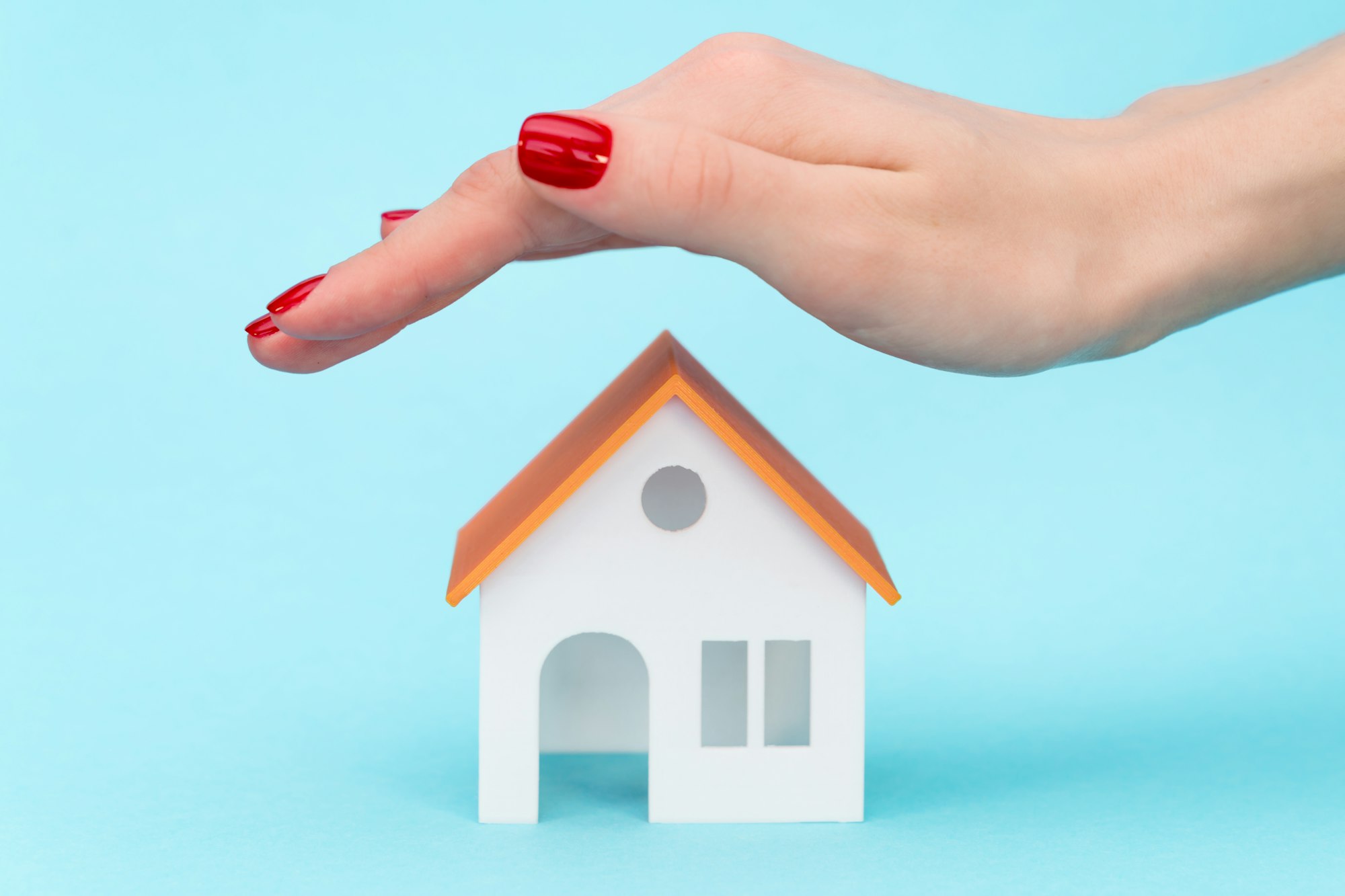 a woman's hand over the roof of the toy house on a blue background with free space for text